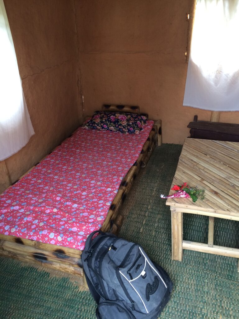 Pink cot on bamboo bed frame with grey backpack leaning against the bed.